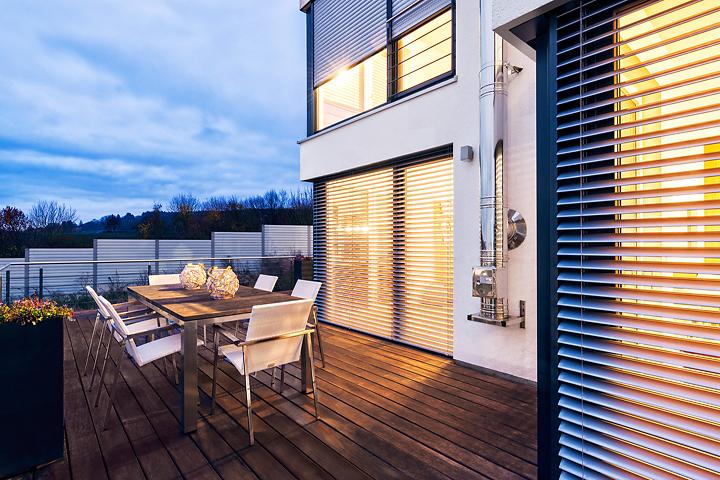 Terrasse mit Tischgruppe bei Dämmerung mit Blick auf Raffstoren